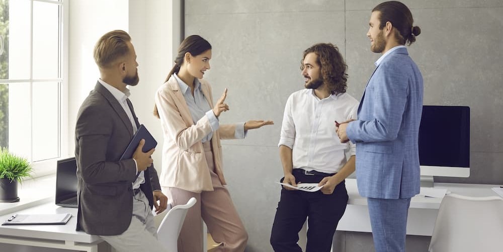 Eine Gruppe von vier Geschäftspersonen steht in einem modernen Büro und führt ein Verkaufsgespräch