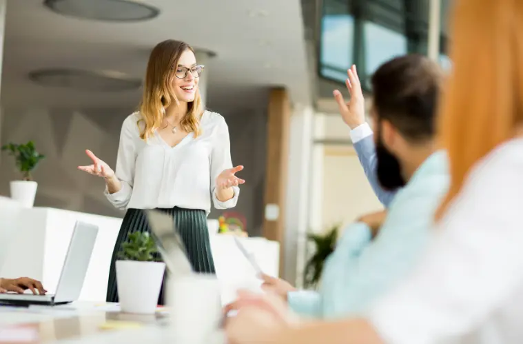 Eine Sales Representative steht vor Mitarbeitern eines Kunden, die an einem Tisch sitzen, und beantwortet im Rahmen einer Präsentation eine Zwischenfrage.
