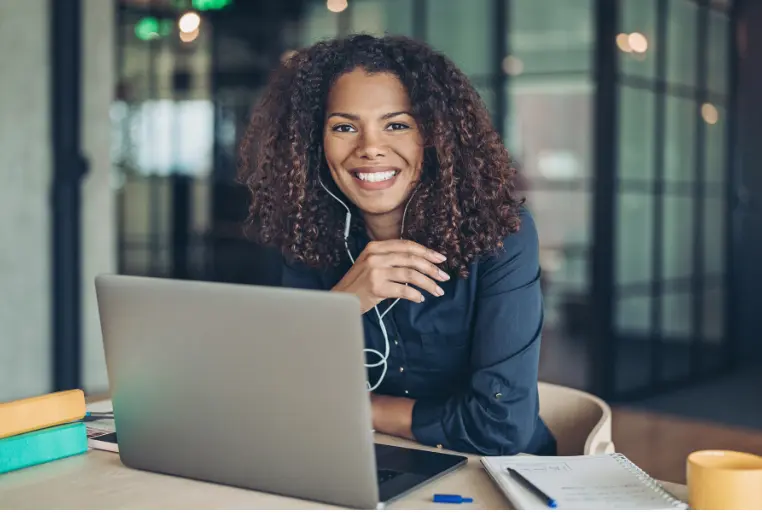 "Inside Sales Managerin bei der Arbeit. Eine junge Frau sitzt in einem modernen Büro an ihrem Laptop und schaut lächelnd in die Kamera."
